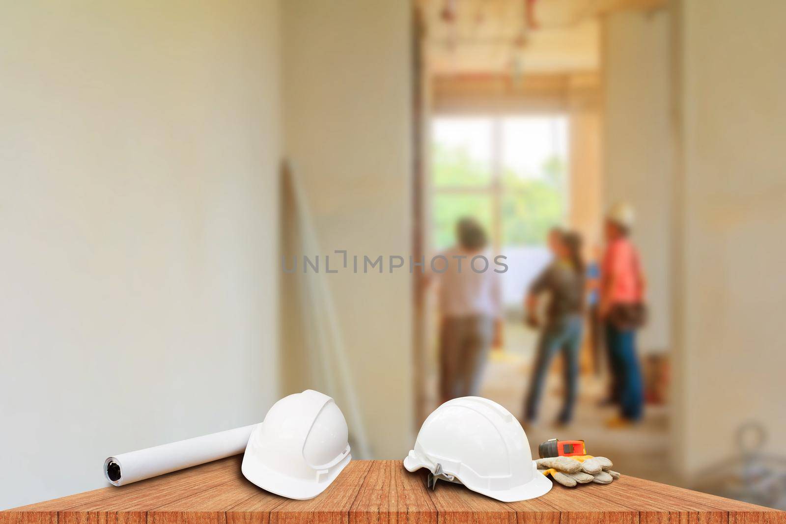 two white safety helmet and leather glove Measuring Tape, roll paper plan blueprint for engineering working interior construction site building on wood floor table with copy space add text. blur background