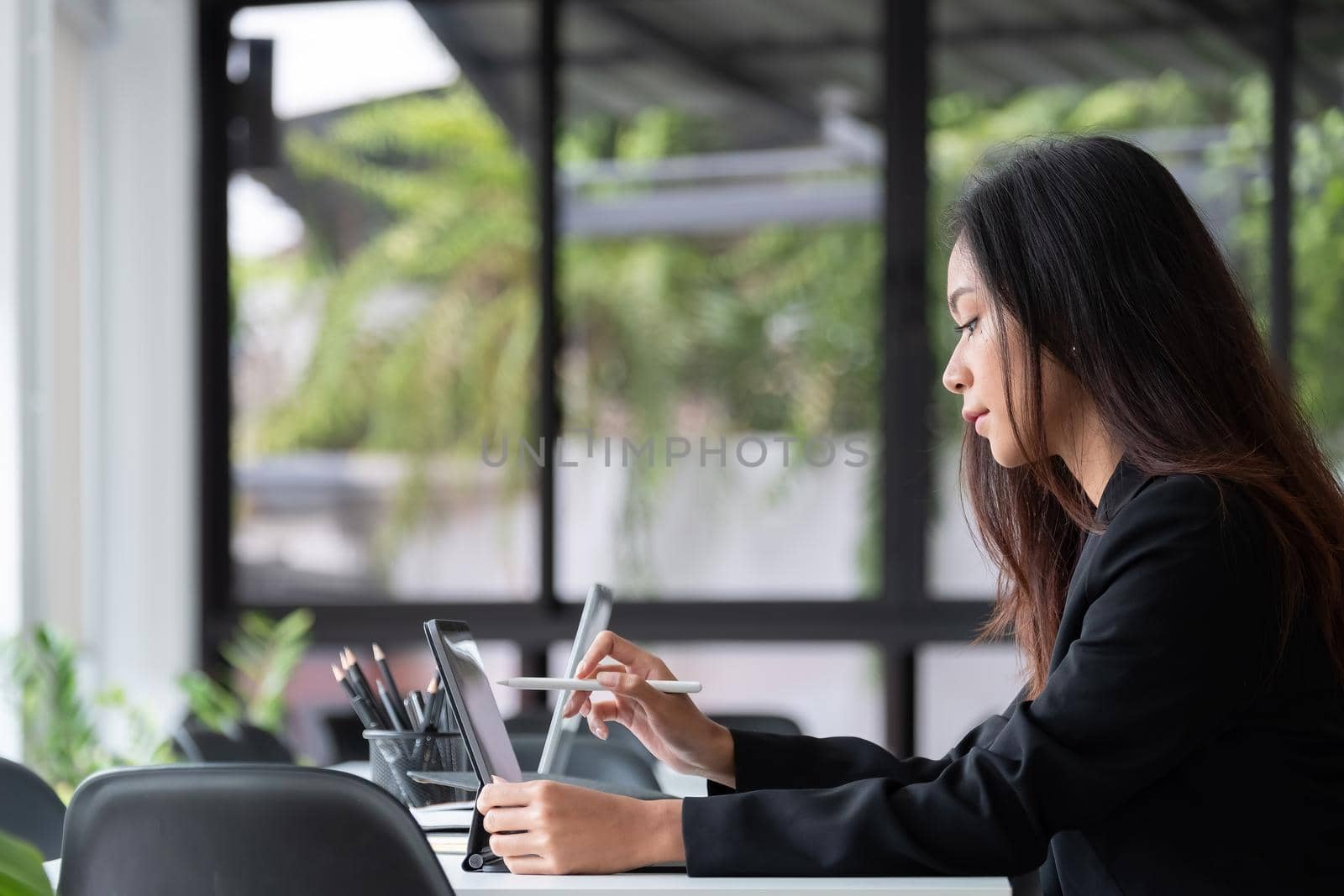 Young asian woman using digital tablet with pen stylus while sitting at her office desk in modern office by nateemee