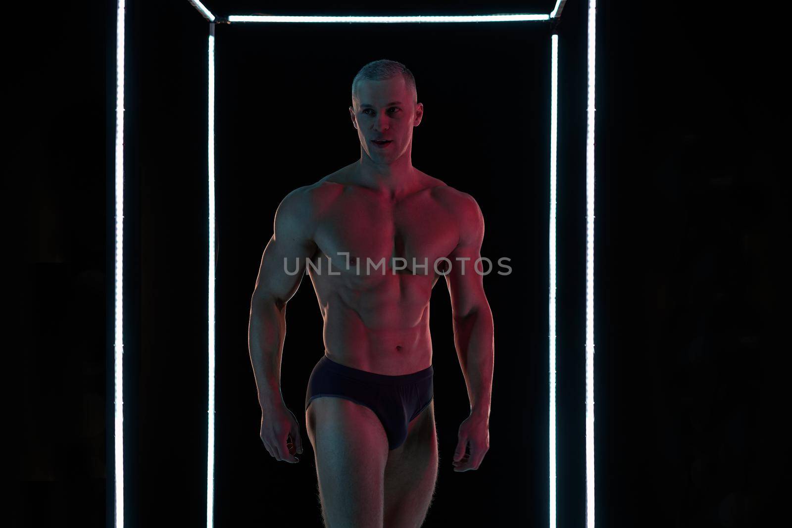Active lifestyle concept. Professional bodybuilder showing perfect muscular body, neon lamps illumination on background Sport and fitness concept