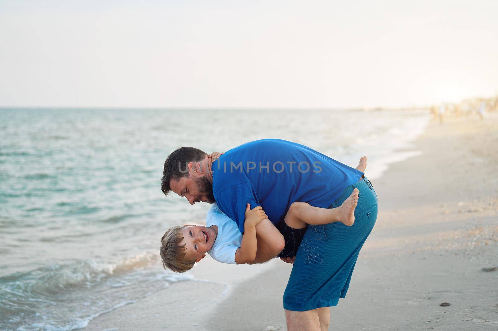 Father son spending time together sea vacation Young dad child little boy walking beach Fathers day. Family with one child. Happy childhood with daddy. sitting on hands laughs