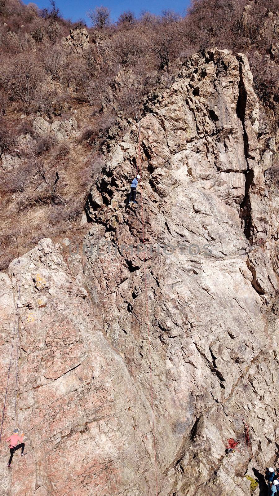 A group of people are engaged in rock climbing. High steep cliff. With the help of a rope, insurance and a partner, climbers climb to the top. Winter time of the year, sometimes there is snow.