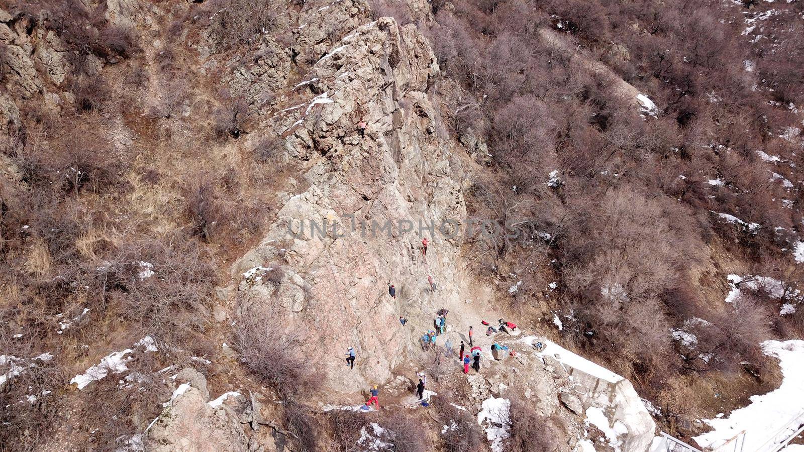 A group of people are engaged in rock climbing. High steep cliff. With the help of a rope, insurance and a partner, climbers climb to the top. Winter time of the year, sometimes there is snow.