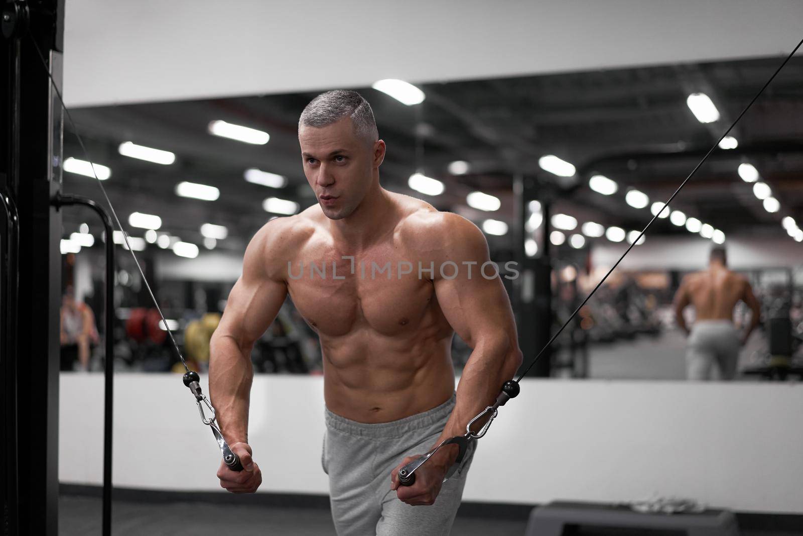 Muscular athletic bodybuilder standing training chest and shoulders muscles on fitness equipment wire cable machine Sport fitness healthy lifestyle Man do flyes exercises on gym machine
