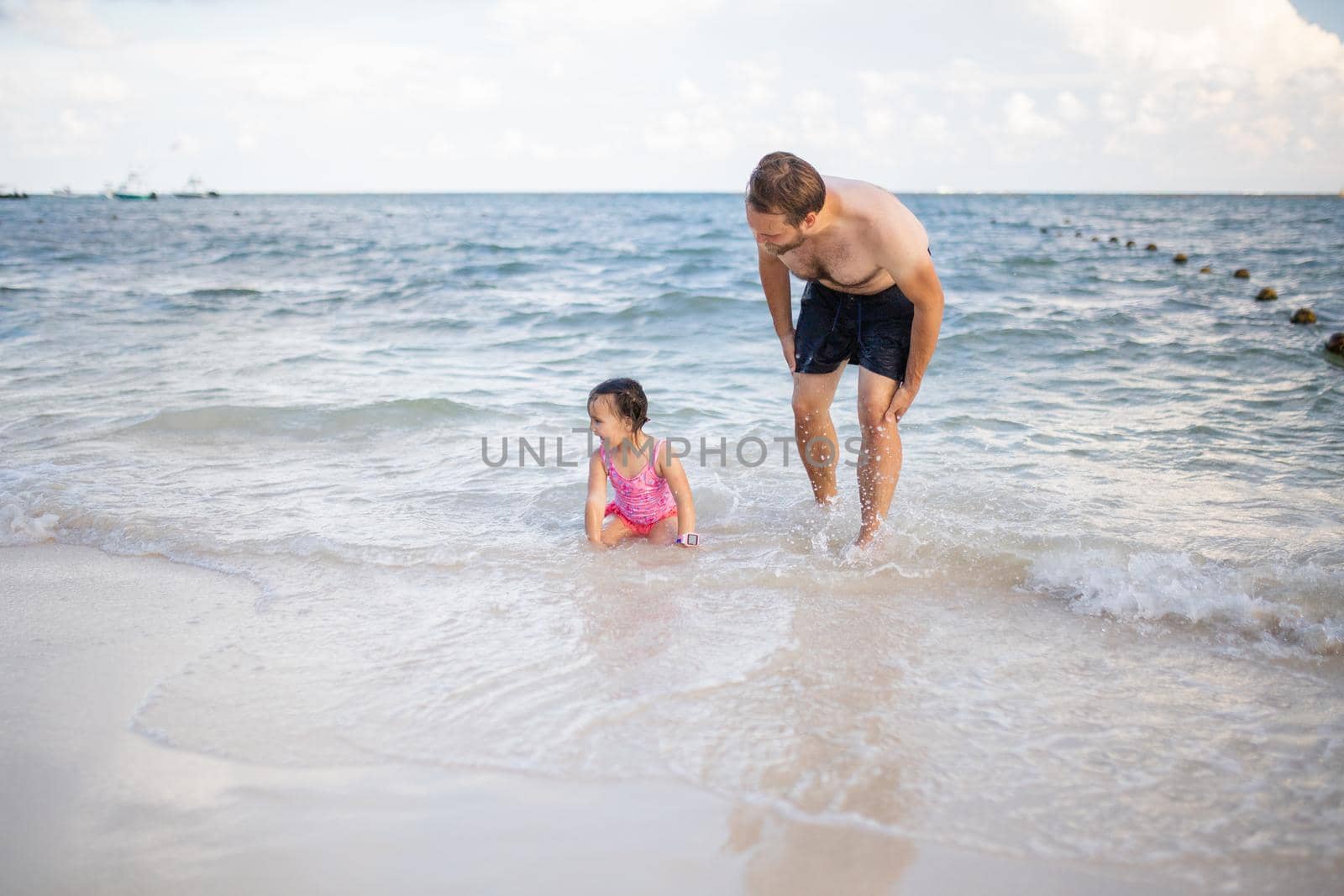 Happy father and young daughter joyfully playing in the water at the beach. Man and cute young child having fun in sea. Tropical summer vacations