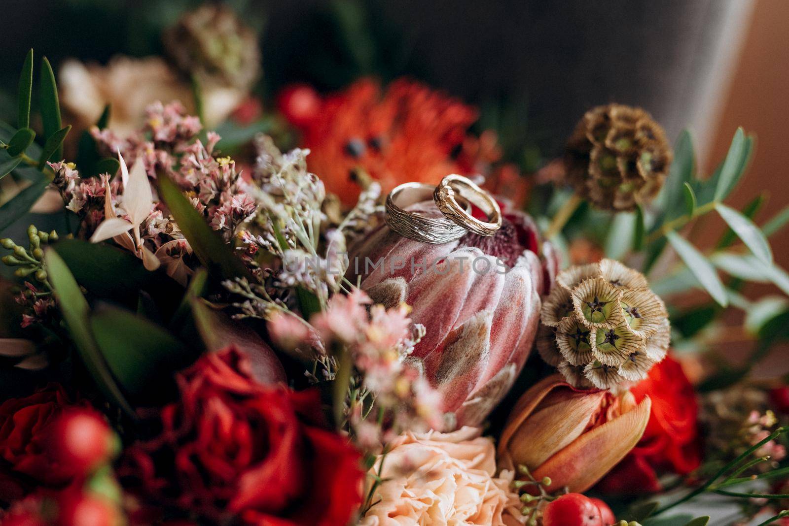 Gold wedding rings licked under the bark of a tree on a red wedding bouquet