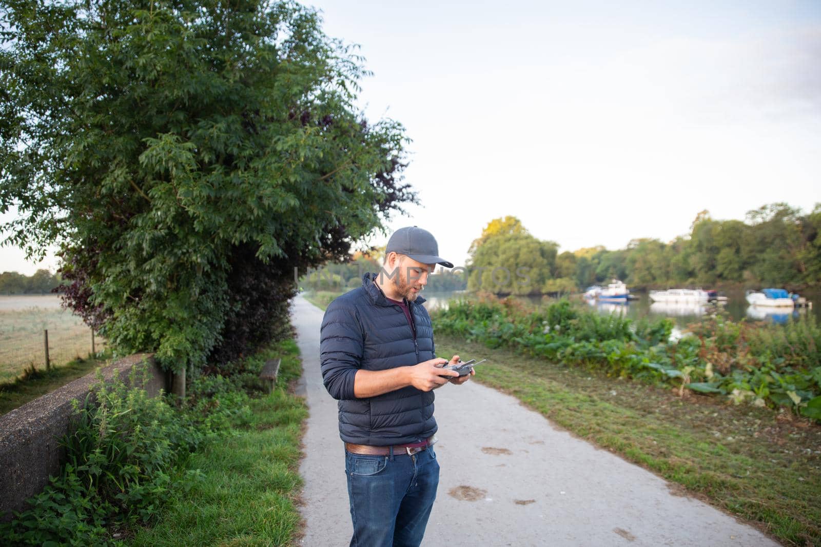 Concentrated man standing on path holding remote control in park. Man in park with trees and boats on lake as background. People interacting with technology outside