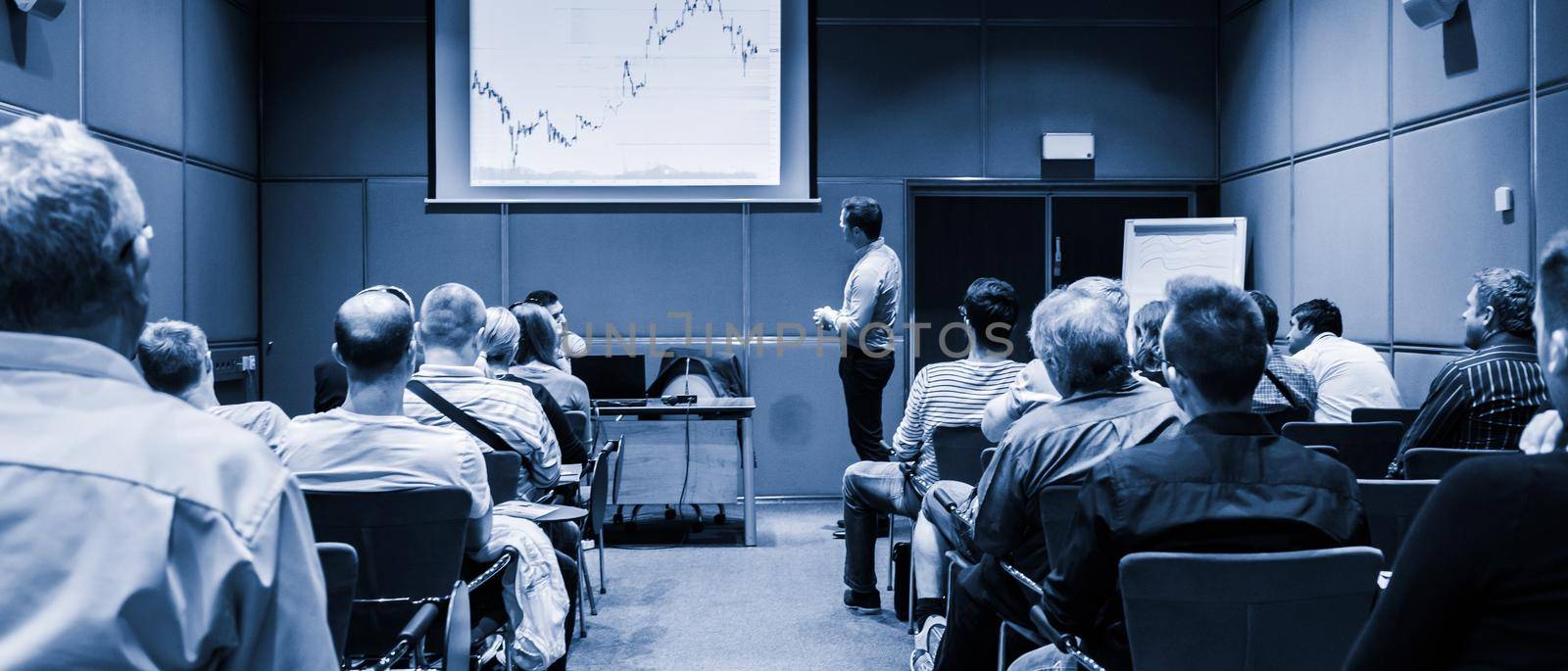 Speaker giving a talk in conference hall at business event. Unrecognizable people in audience at conference hall. Business and Entrepreneurship concept. Blue toned black and white.