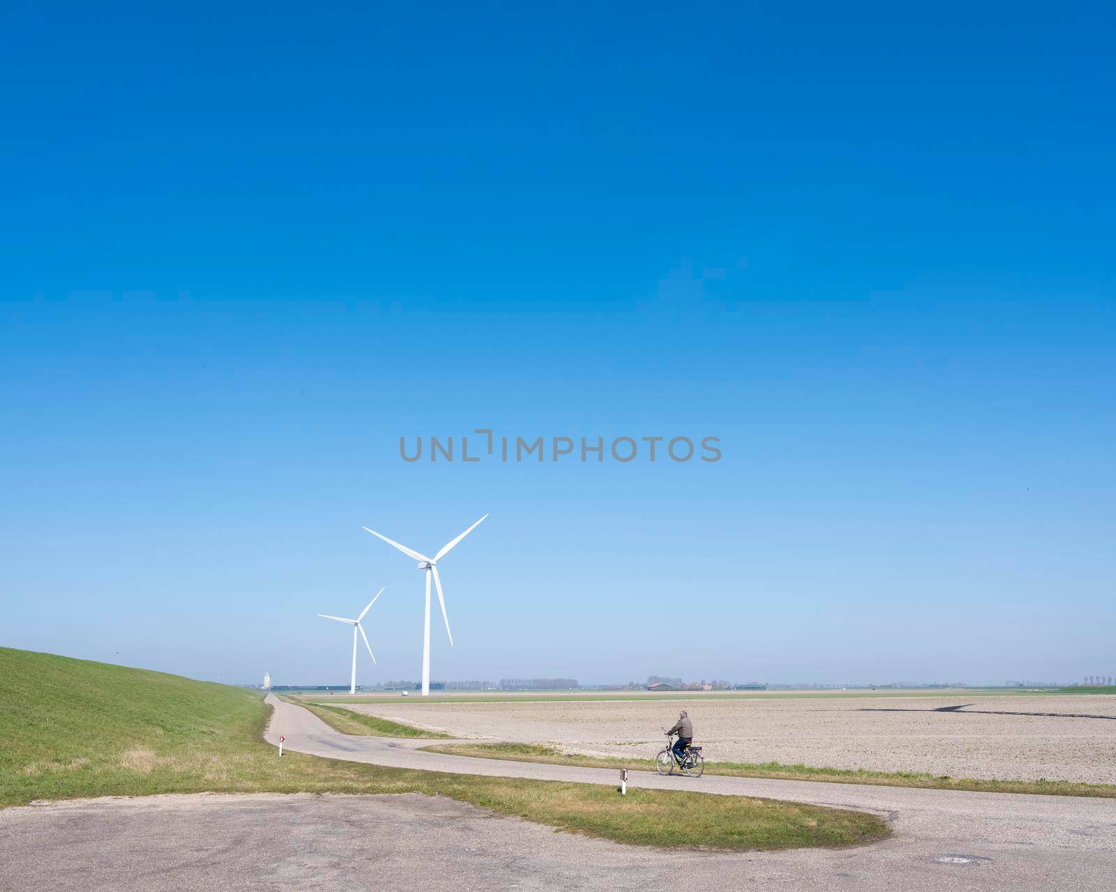 zierikzee, netherlands, 30 march 2021: man on bicycle and wind turbines in rural landscape of schouwen duiveland in dutch province of zeeland under blue sky