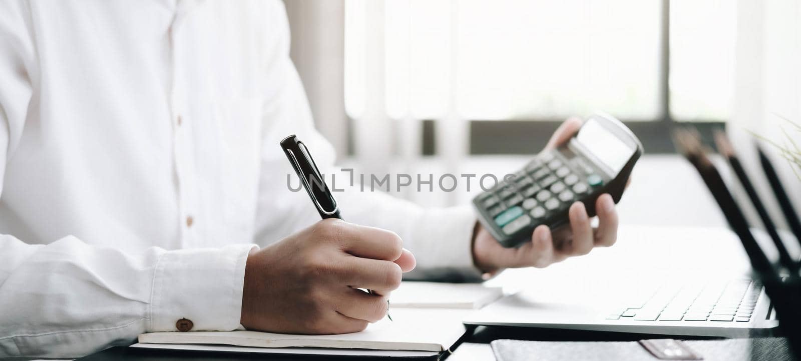 Close up Business man using calculator and laptop for do math finance on wooden desk in office and business working background, tax, accounting, statistics and analytic research concept.