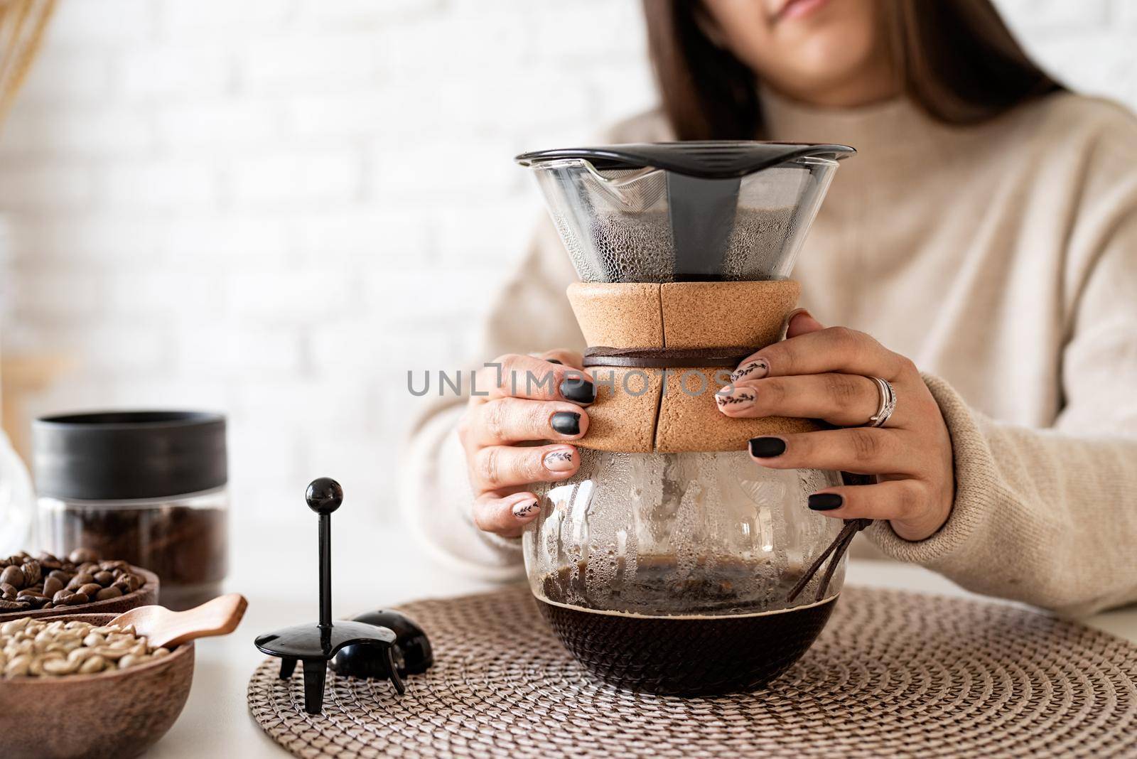 Alternative coffee brewing. Young woman brewing coffee in coffee pot standing at the white table with various stuff for alternative coffee brewing, pouring hot water into the filter