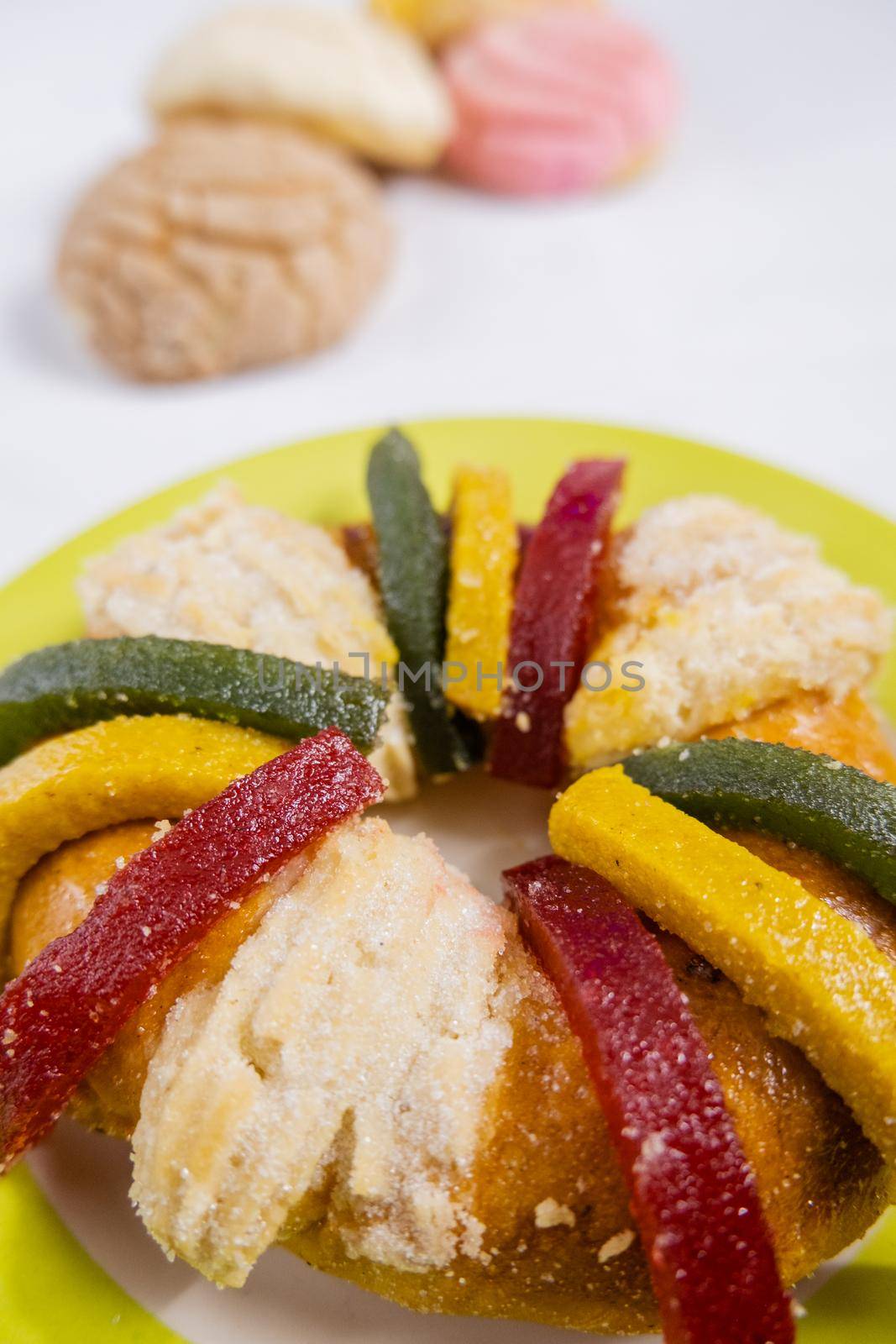 Colorful kings day bread on yellow plate with sweet bread known as concha as background. Classic round Mexican bread with fruit paste slices above white table. Traditional Mexican desserts