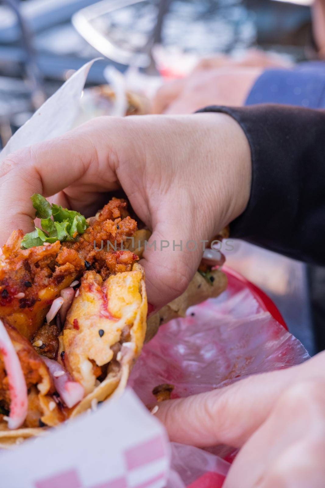 Female hand holding vegetarian taco with onion and lettuce above plastic basket. Woman holding vegan taco al pastor above paper with chessboard texture. Traditional Mexican cuisine