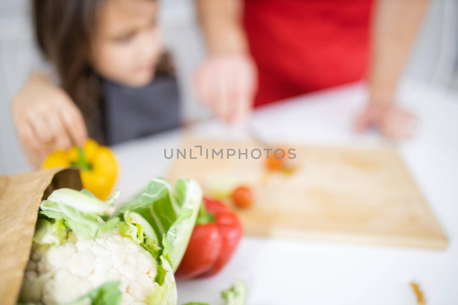 Blurry little girl and her father slicing cherry tomatoes on cutting board. Man helping young child cutting vegetables on wooden board. Daughter-father cooking together