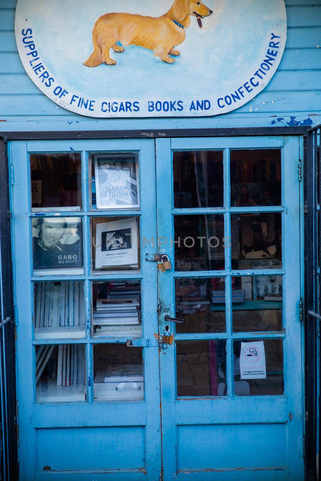 London, UK - February 14, 2020: Books through the blue door of blue British bookstore. Dog smoking cigar on sign above entrance of English bookstore. Peaceful London neighborhood