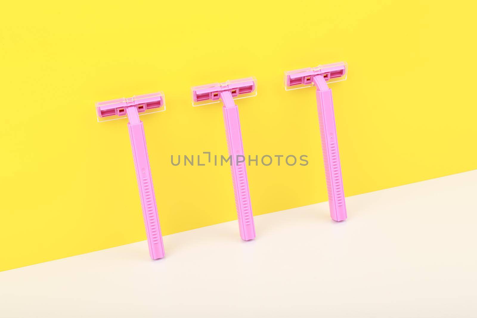 Pink razors on white table against yellow wall. Tools for shaving concept by Senorina_Irina