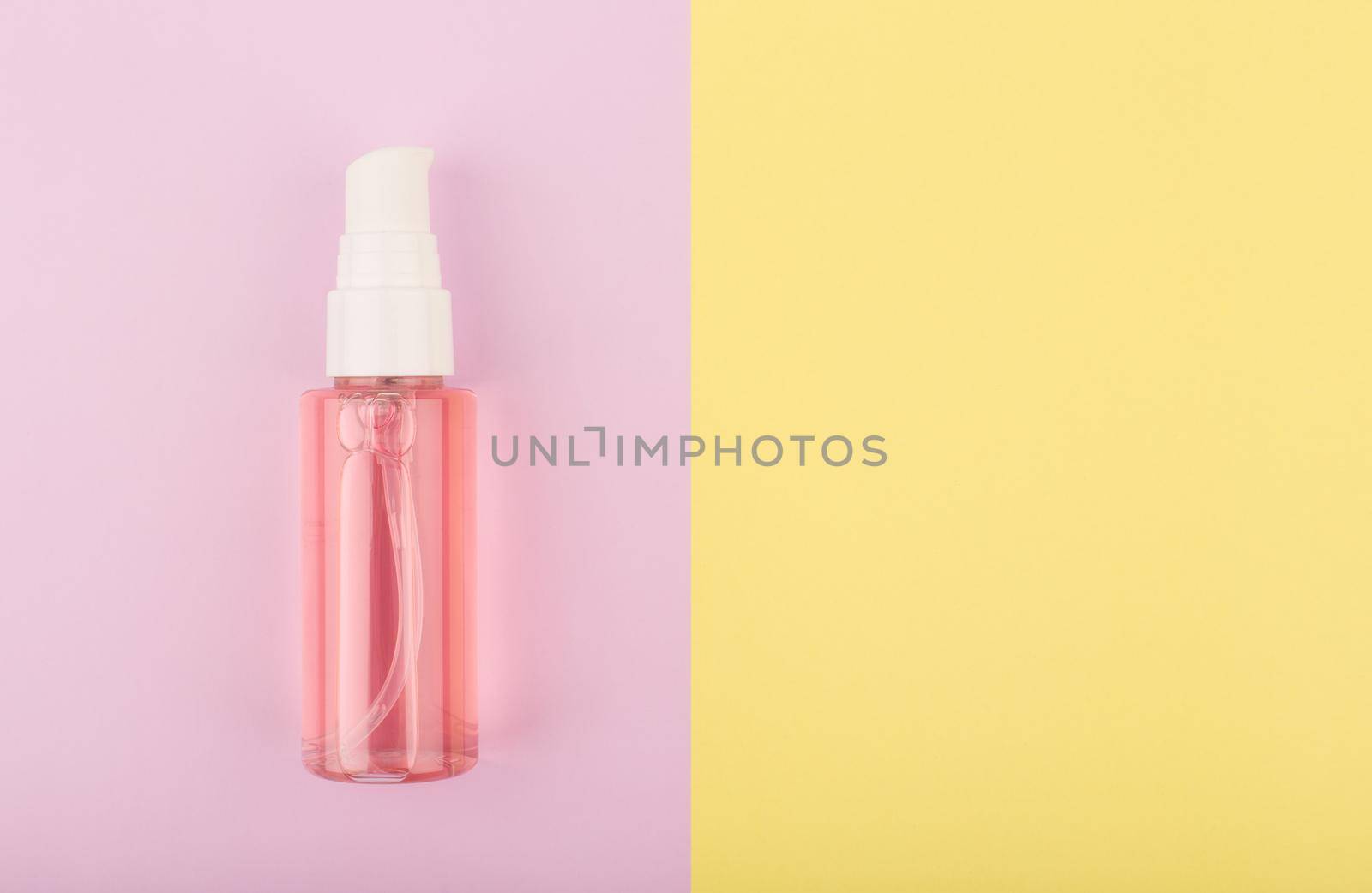 Foam or gel for skin cleaning and exfoliating in transparent tube with dispenser on pink and yellow background with copy space. Concept of skin care products for every day use