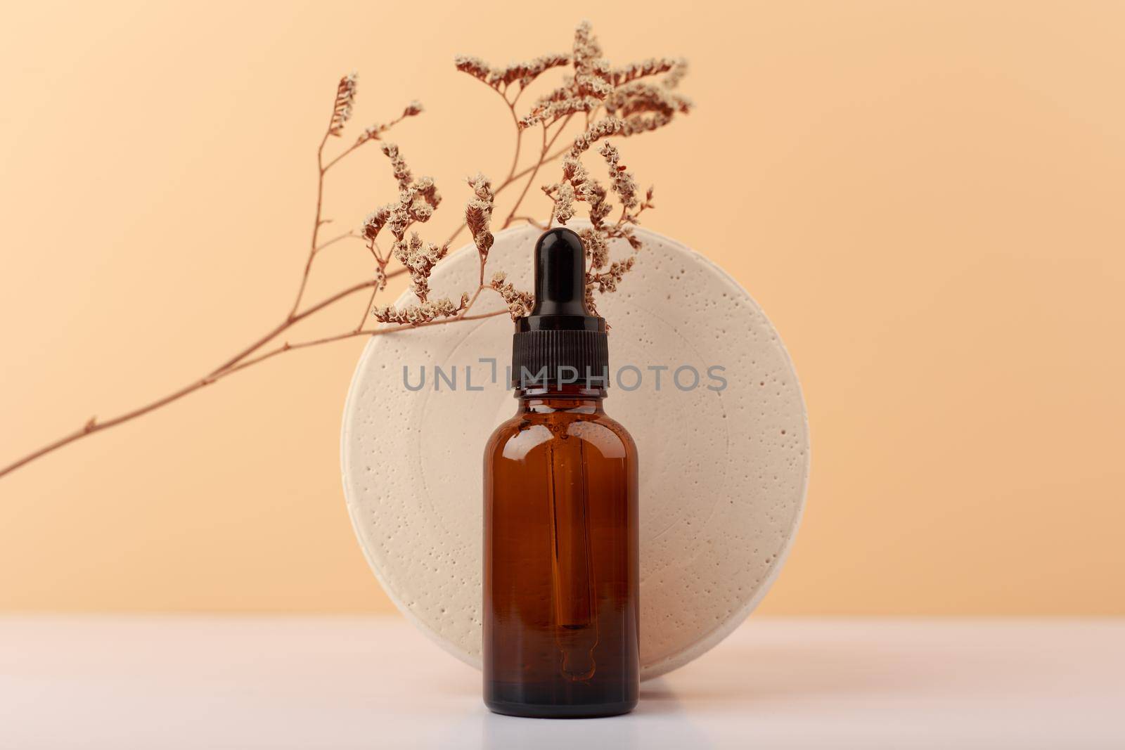 Selective focus, skin serum against round podium with dry plant on white table against beige background with copy space. Concept of anti aging skin treatment