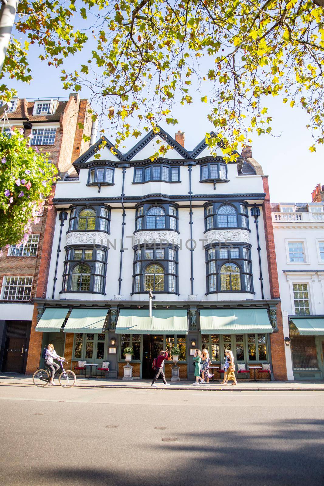 British restaurant building on the other side of the street with people passing by. Beautiful white English building with Victorian architecture. Classic London architecture