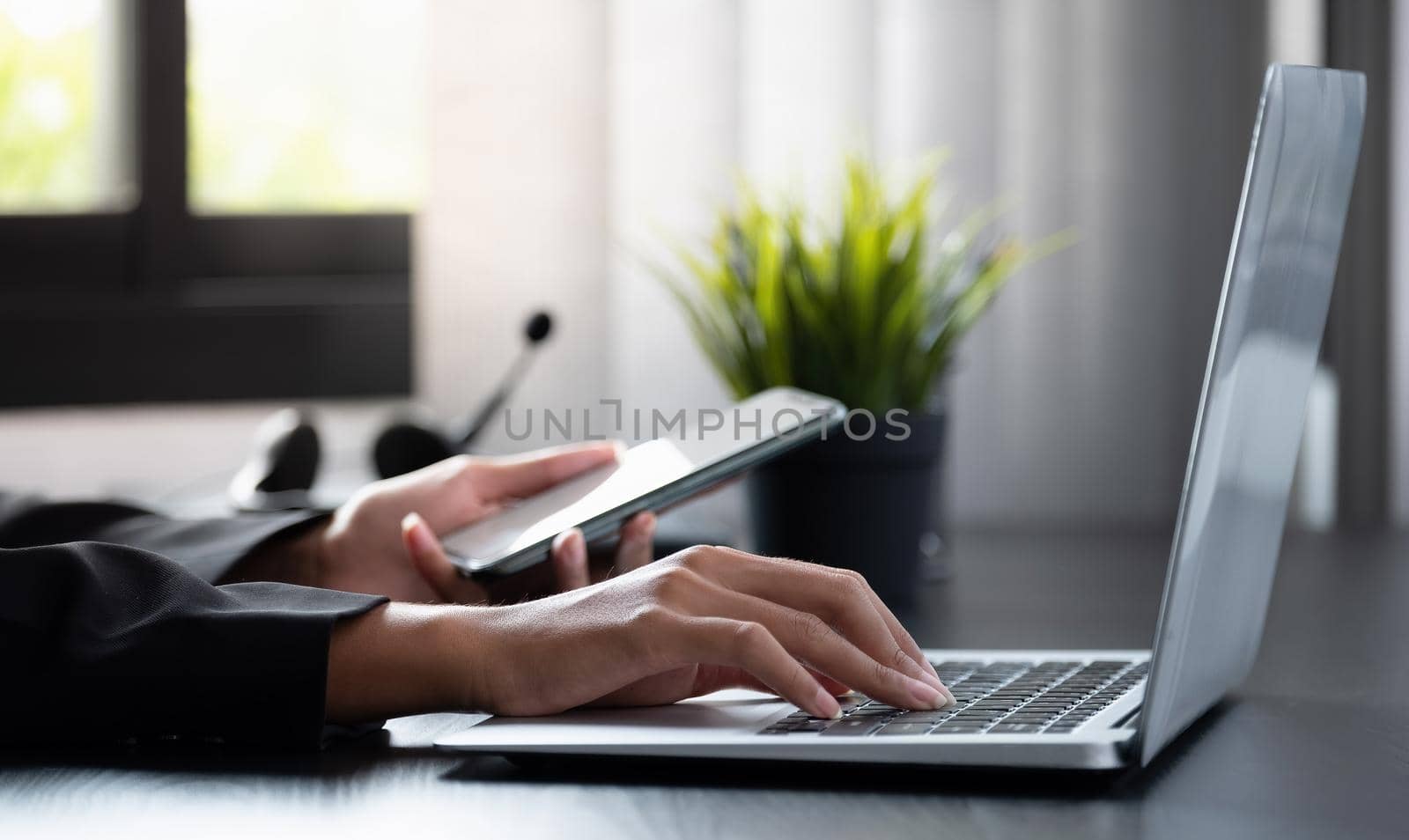 Businesswoman working on computer. Female using smart phone and laptop in the office. Internet marketing, finance, business concept