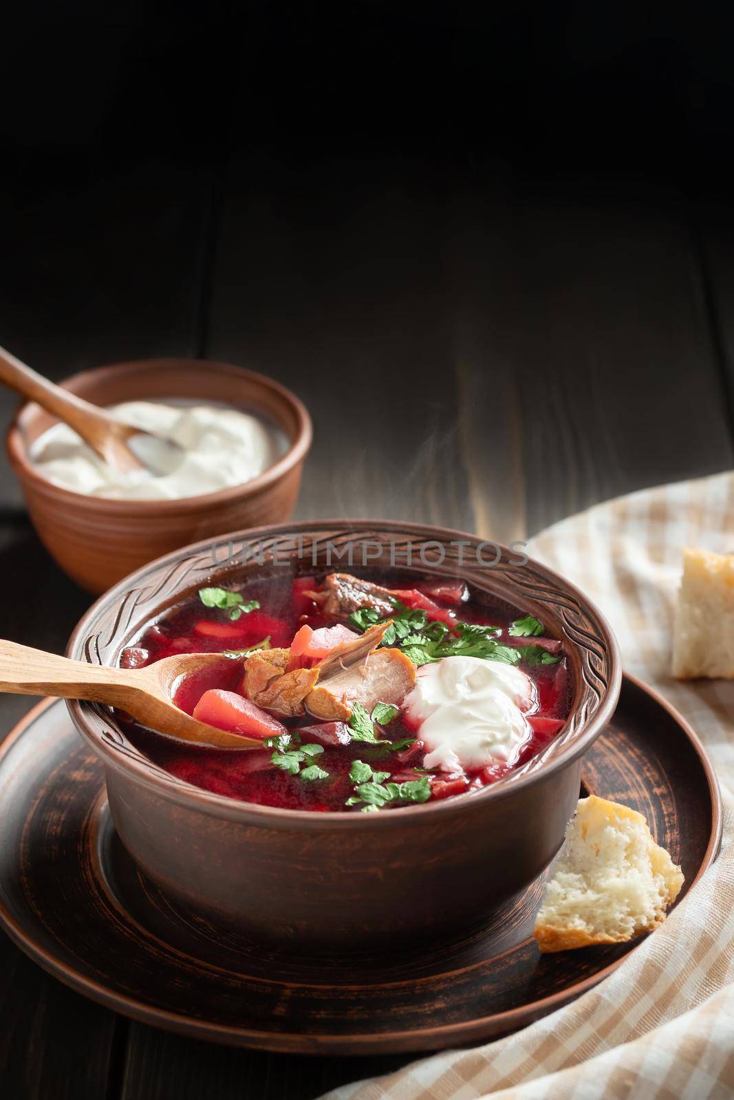 Freshly cooked borscht - traditional dish of Russian and Ukrainian cuisine in earthenware dish with bacon, sour cream and garlic, vertical image by galsand