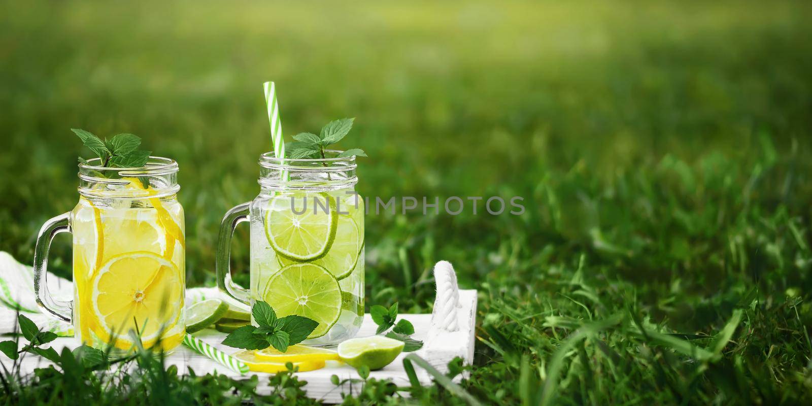 Cold refreshing homemade lemonade with mint, lemon and lime in mason jars on a summer lawn, copyspace.