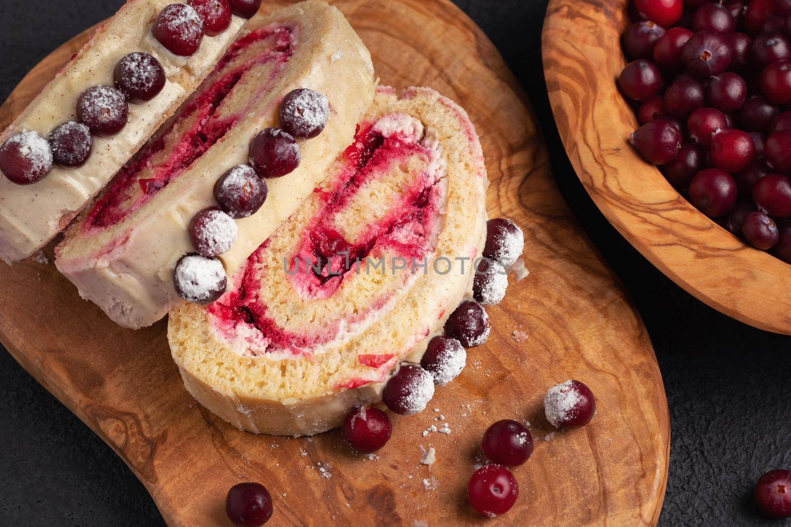 Homemade biscuit sweet roll with cranberries and cream on a black table, top view, flat lay.