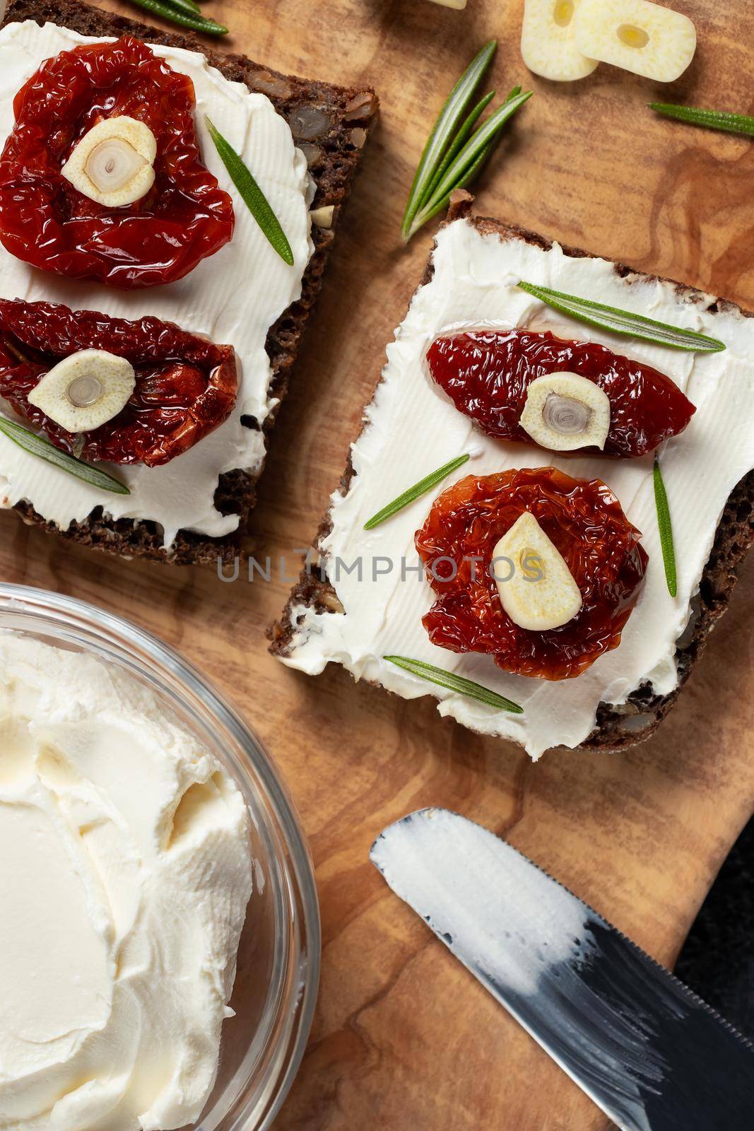 Homemade multigrain bread sandwiches with cream cheese and sun-dried tomatoes on a wooden platter. Healthy eating concept. Vertical image.