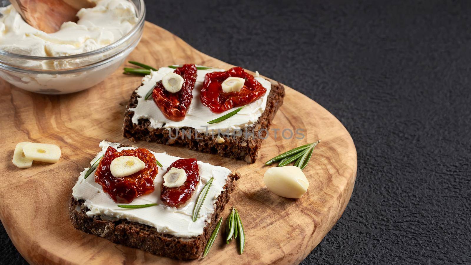 Homemade multigrain bread sandwiches with cream cheese and sun-dried tomatoes on a wooden platter. Healthy eating concept, copy space by galsand