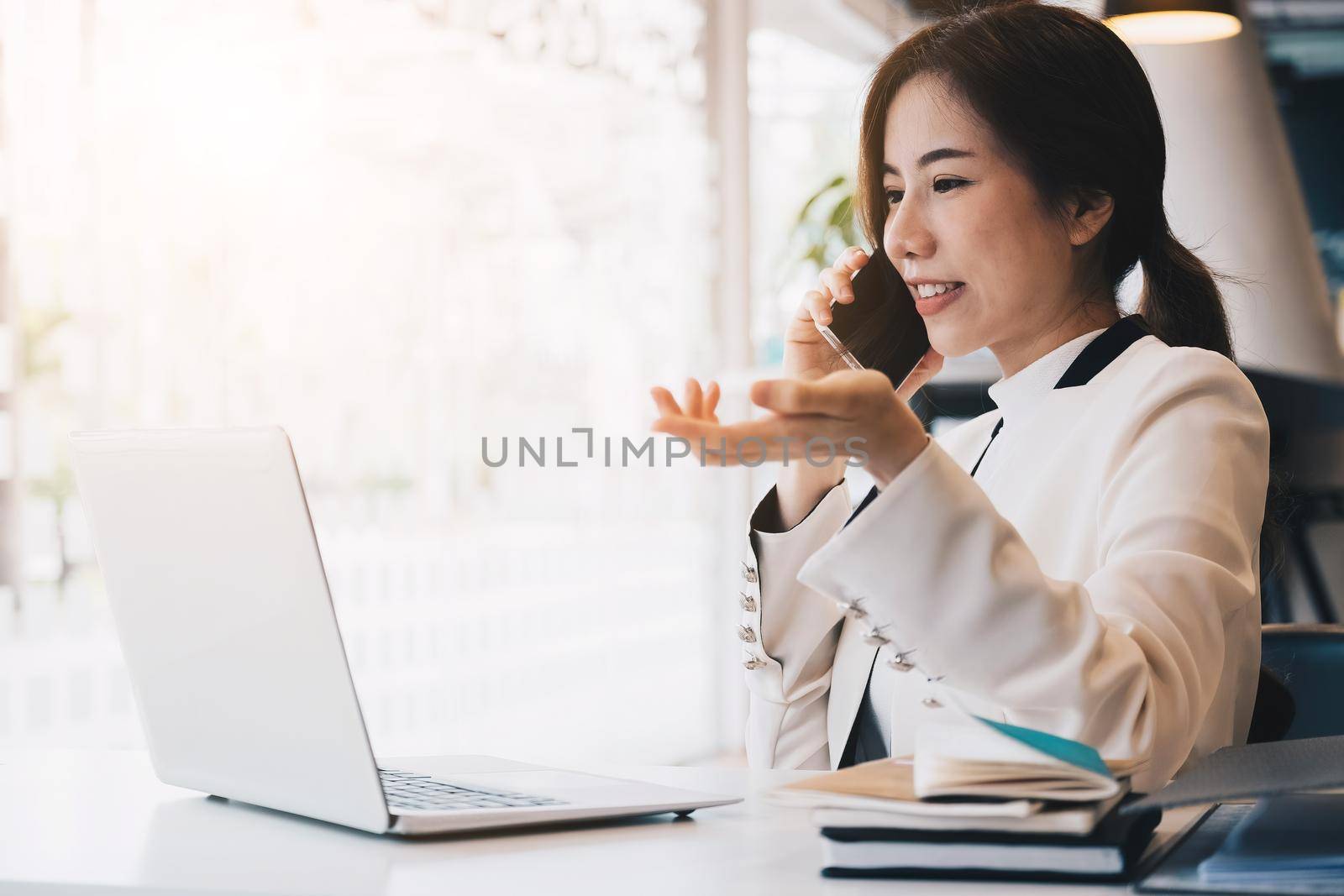 Asian business woman beautiful charming smiling using laptop and talking on phone at her office. by nateemee