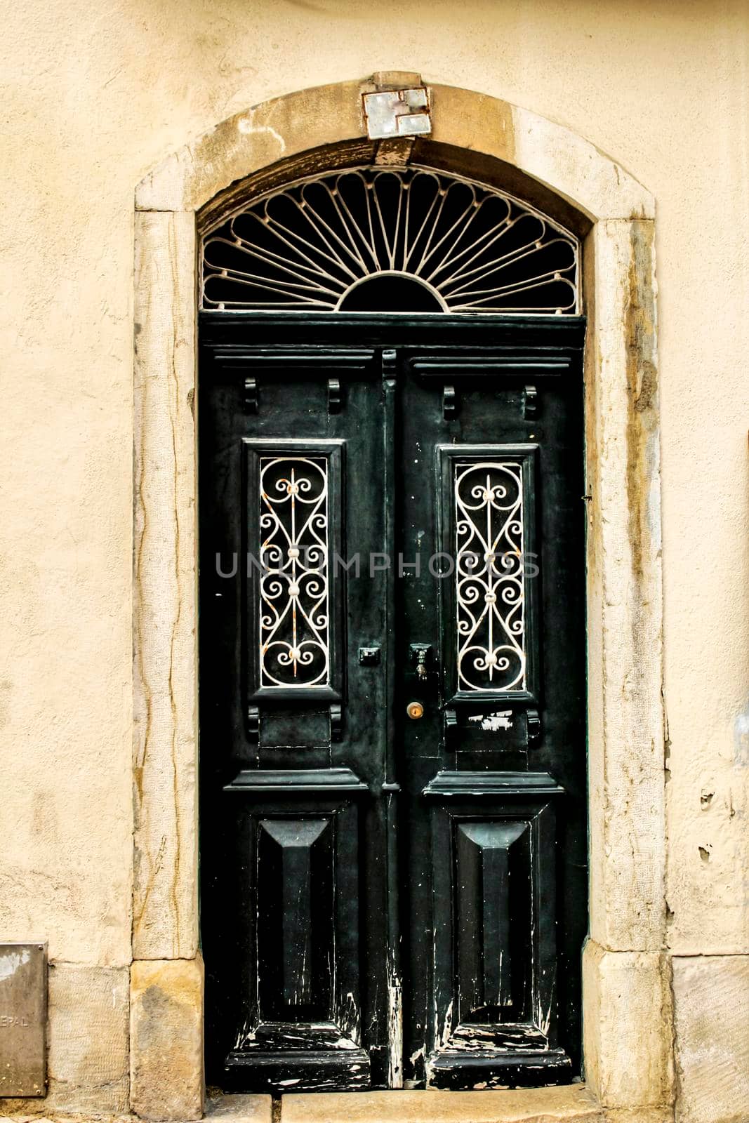 Old wooden door with tiled facade in Lisbon. Wrought metal details on the door.