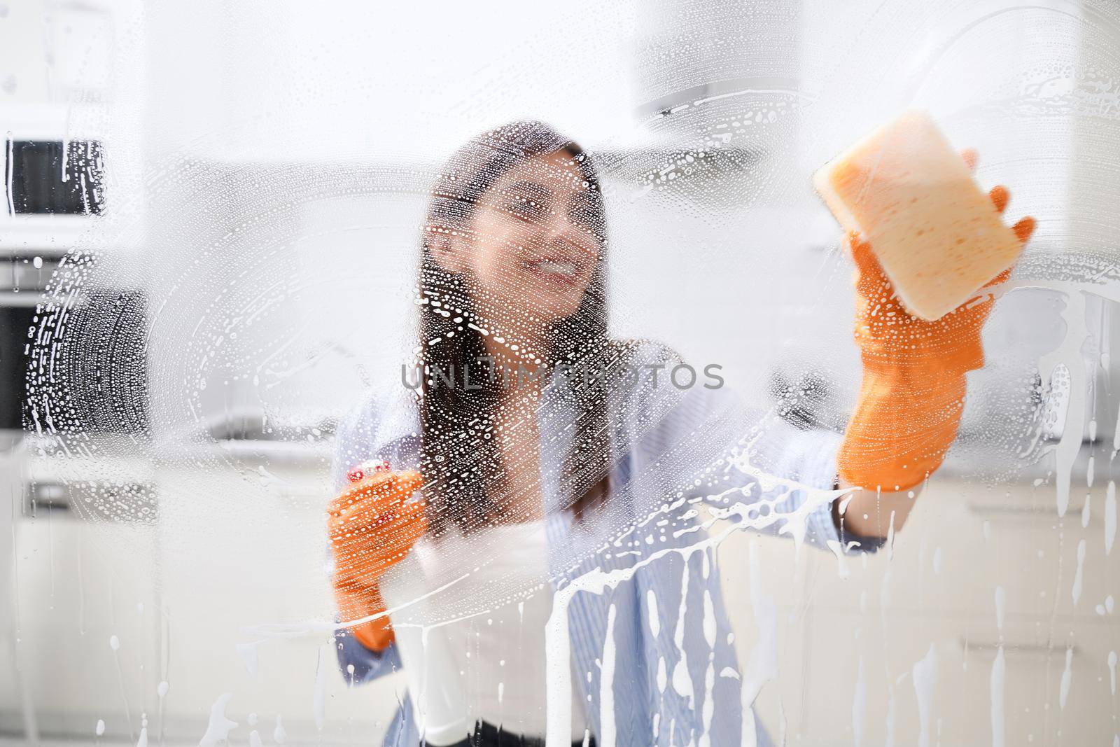 Young woman cleaning dirty window with special detergent. by SerhiiBobyk