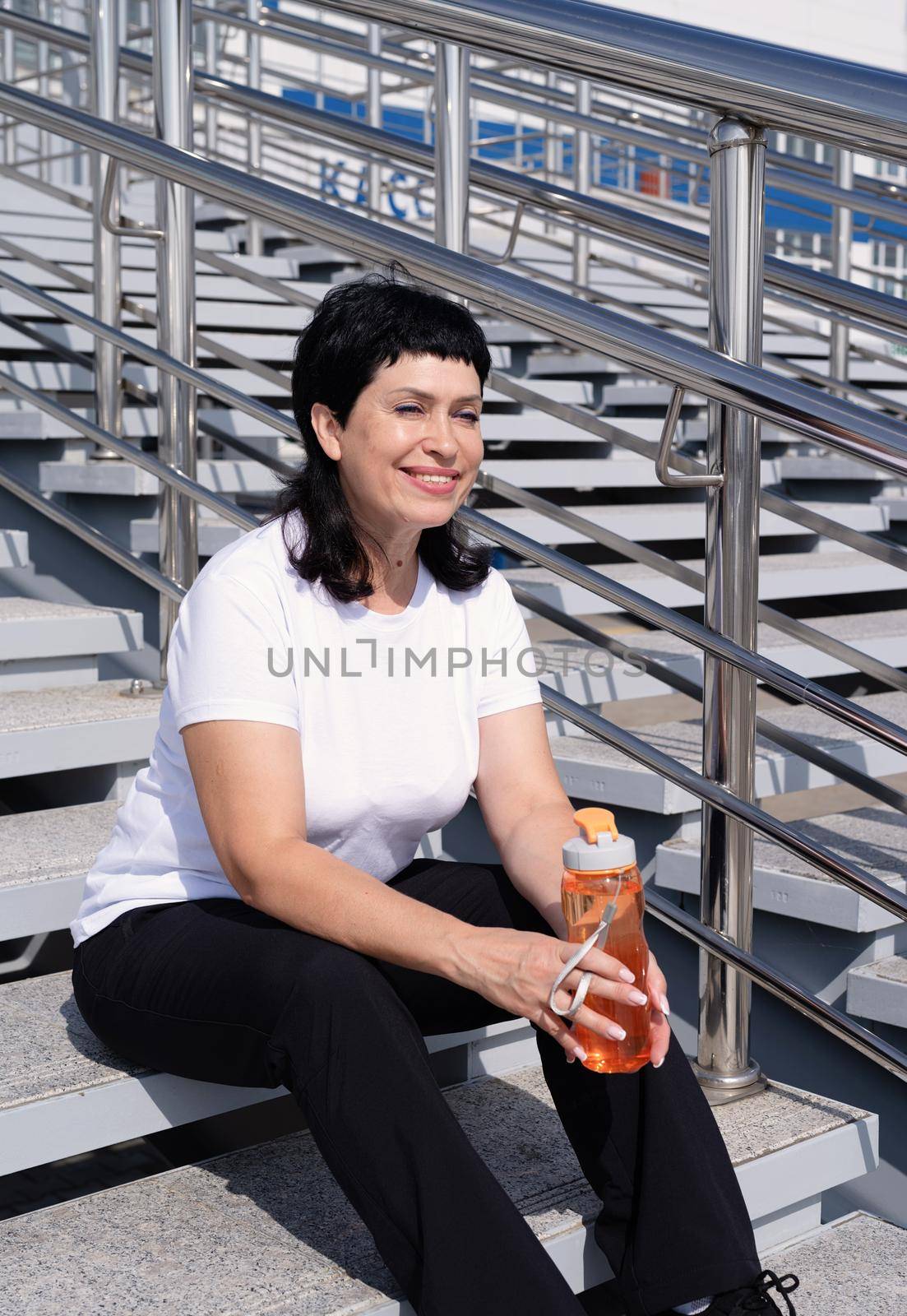 Sport and fitness. Senior sport. Active seniors. Smiling senior woman drinking water after workout outdoors on urban background