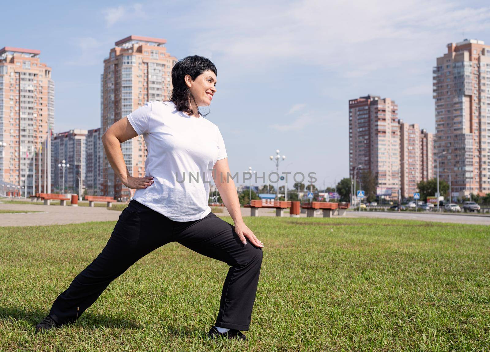 Smiling senior woman warming up stretching outdoors in the park by Desperada