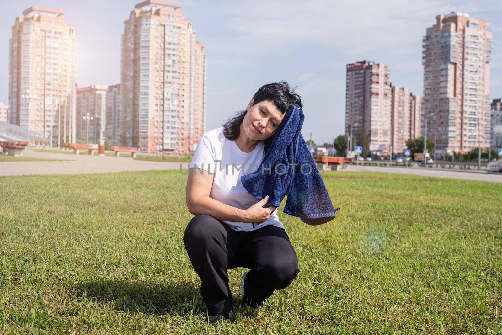 senior woman wiping out sweat after hard workout outdoors in the park by Desperada