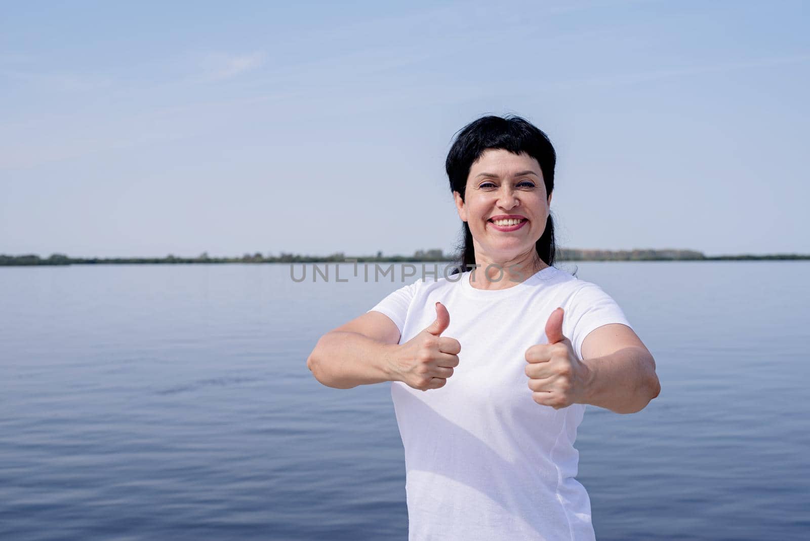 Sport and fitness. Senior sport. Active seniors. Active and happy senior woman in sportswear showing thumbs up working out near the riverside