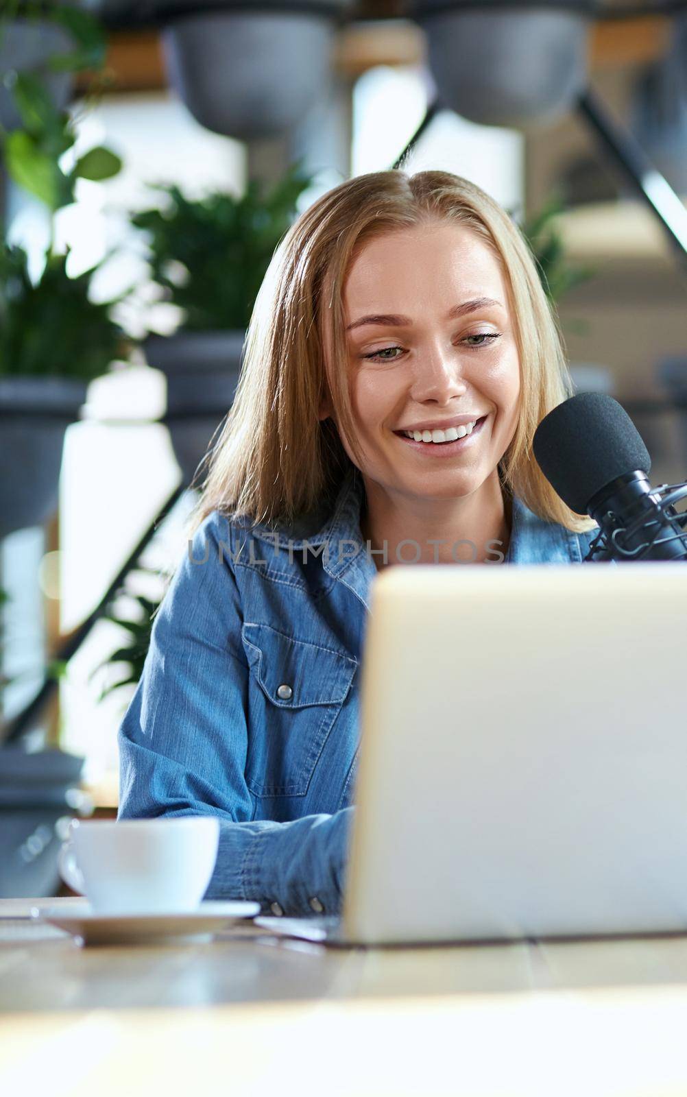 Close up portrait of smiling young attractive woman working in laptop with tasty coffee in cafe. Concept of process communication online in laptop with modern microphone. 