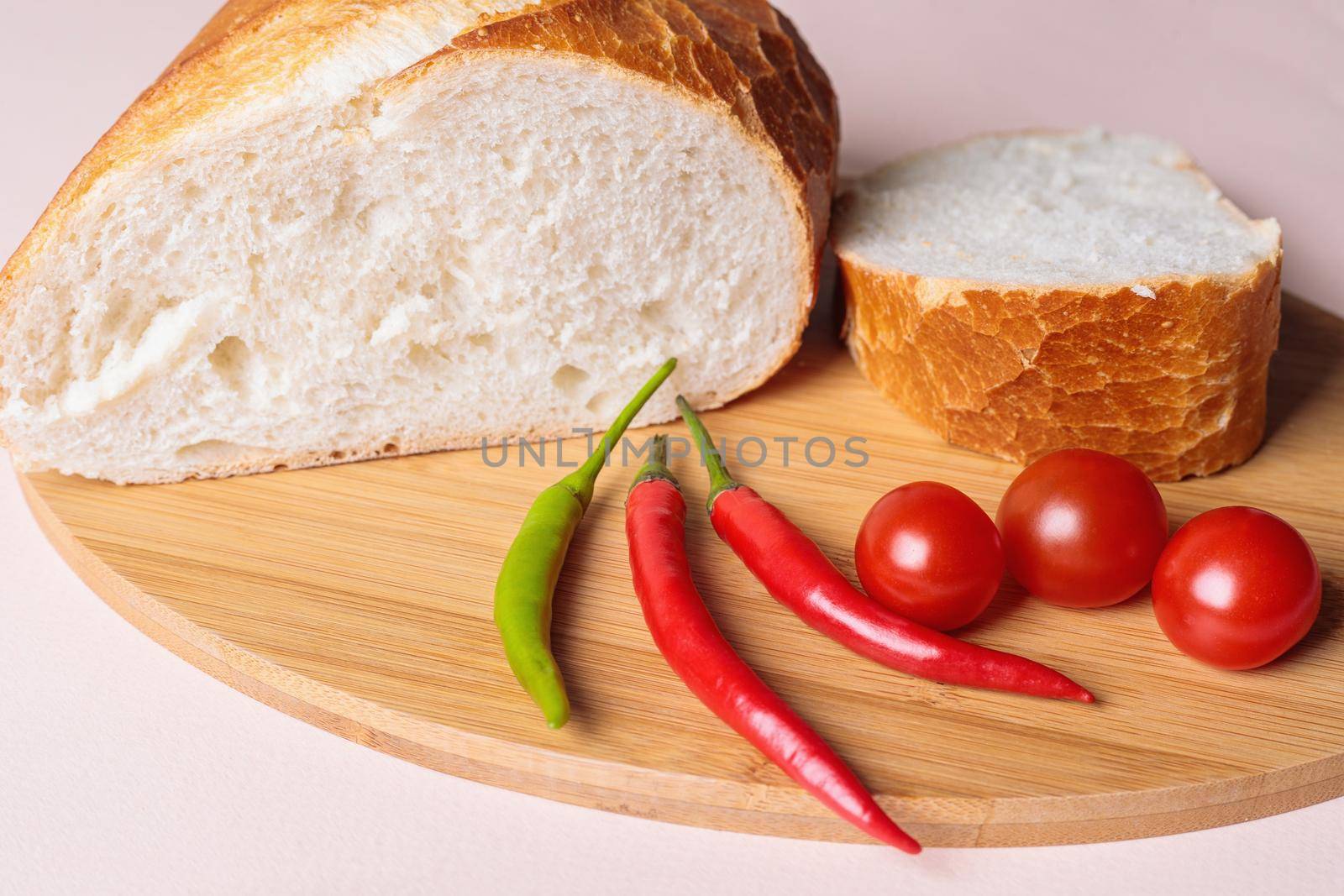 Sliced pieces of white bread with red peppers and tomatoes on a cutting board. Light background