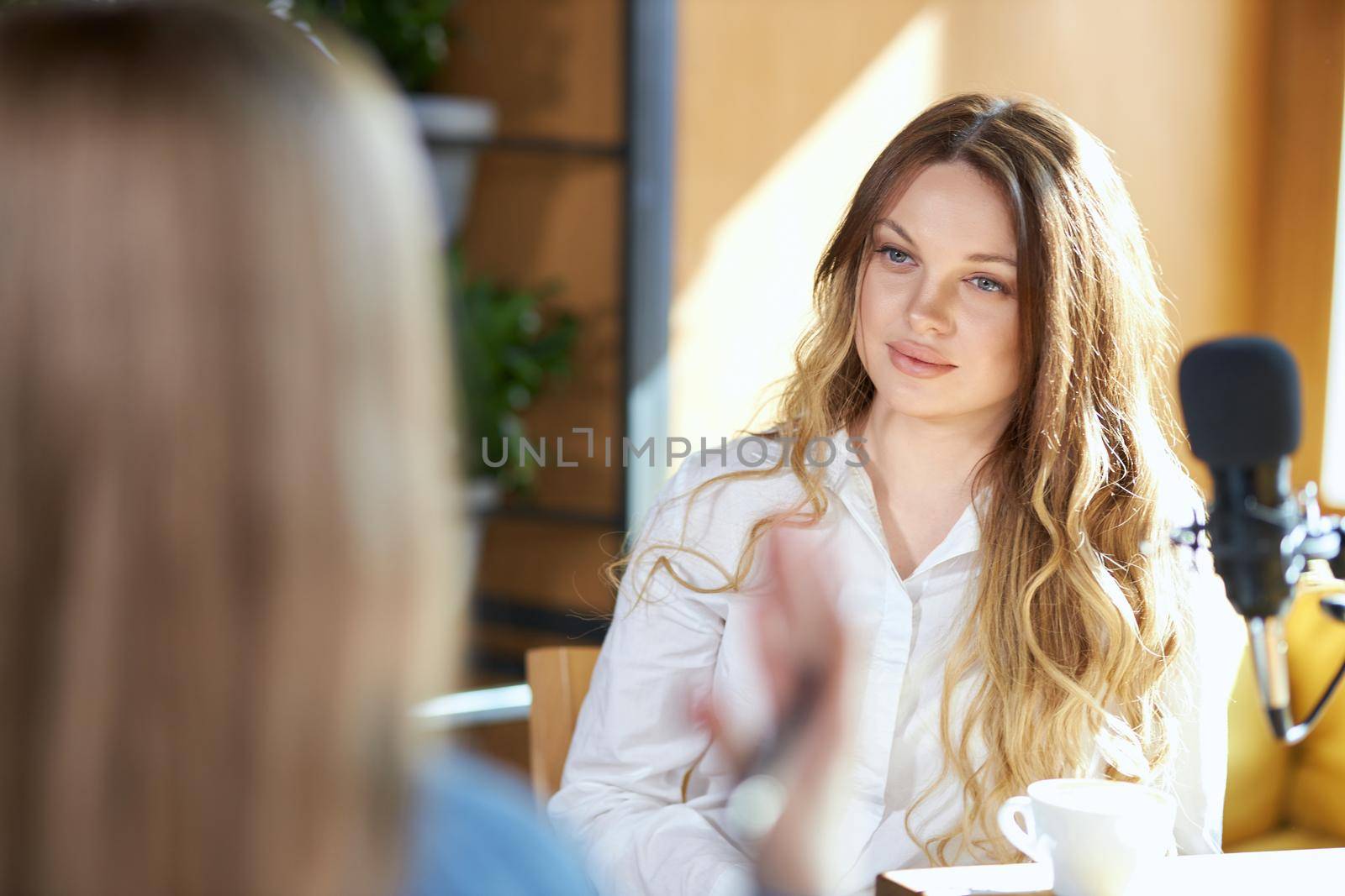 Side view of blogger woman giving interview with modern black microphone with cup coffee. Concept of process communicating about different topics in cafe. 