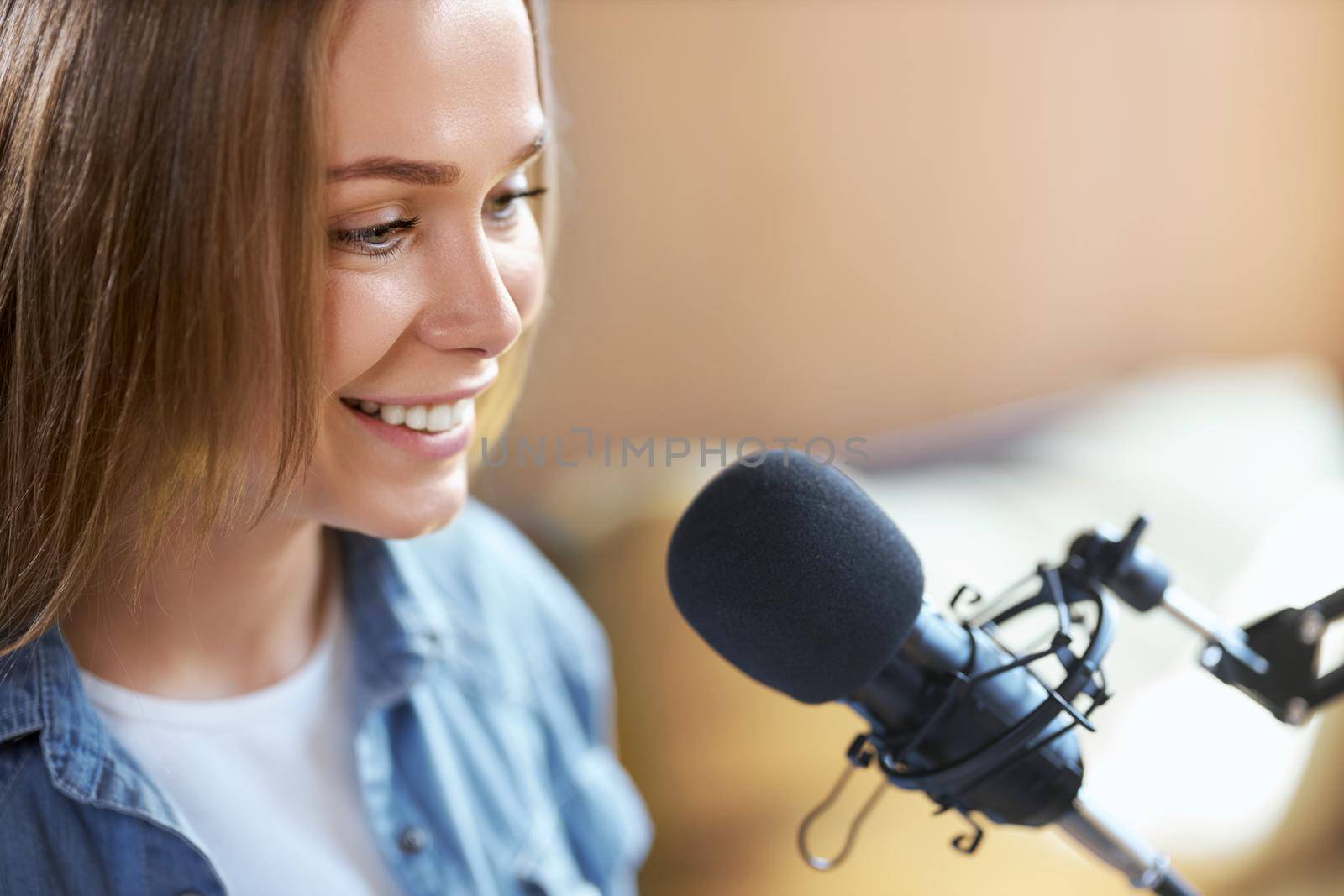 Close up portrait of smiling cute young woman telling interesting information for people in modern microphone. Concept of process communication on radio or live broadcast.