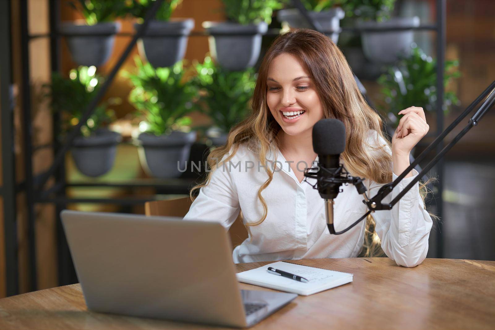 Close up portrait of smiling young blogger woman telling different information online for followers by laptop. Concept of process communicating online with modern microphone and notebook. 