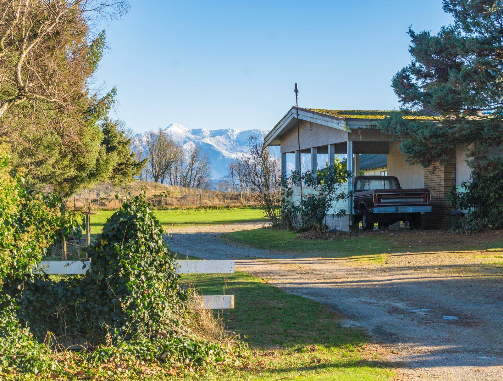 Back yard of family house with old truck parked under carport and mountain view background