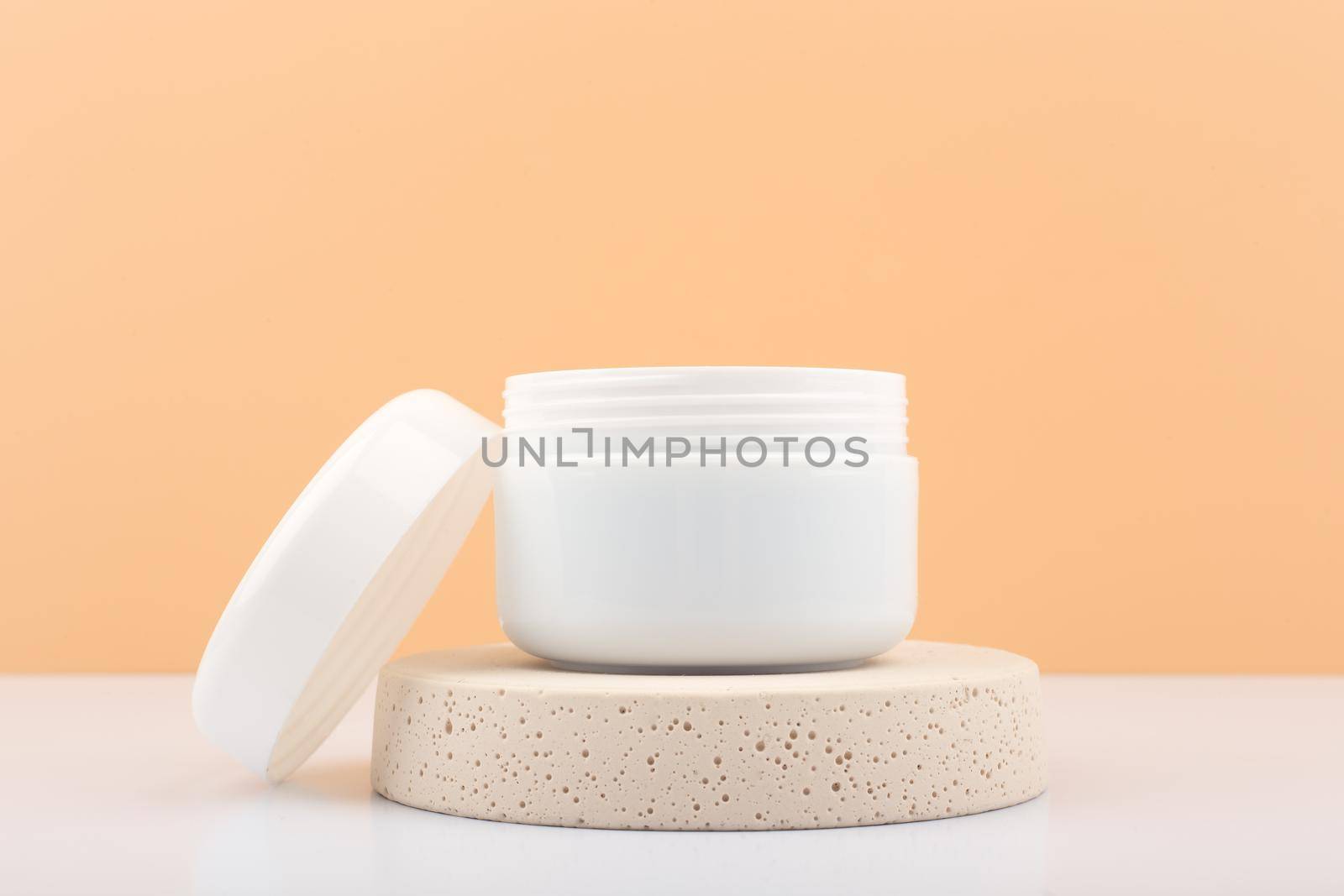 White opened cosmetic jar on beige podium against beige background with palm leaf. Concept of cosmetic products for daily skin or hair care. Jar with scrub, mask or balm.