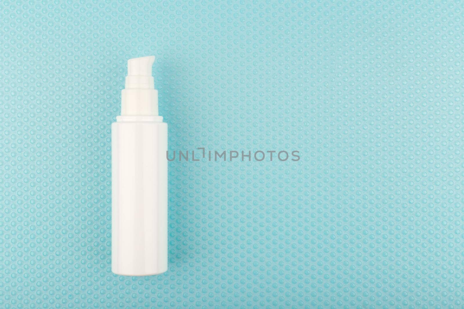 Flat lay with face moisturizing cream or lotion in tall white plastic tube on blue background with bubbles with copy space. Concept of skin treatment for smooth, glowing, young looking skin