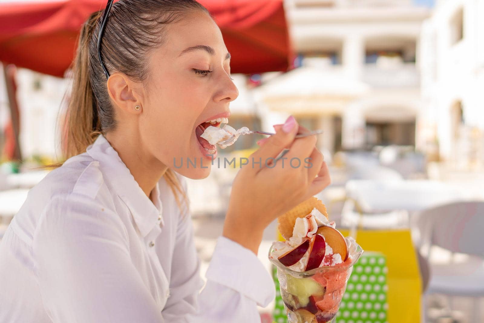 Young beautiful woman takes a break in her shopping day in city eating a big ice cream sitting at cafe bar dehore. Vices and pleasures of modern times from sweets to consumerism of compulsive shopping by robbyfontanesi