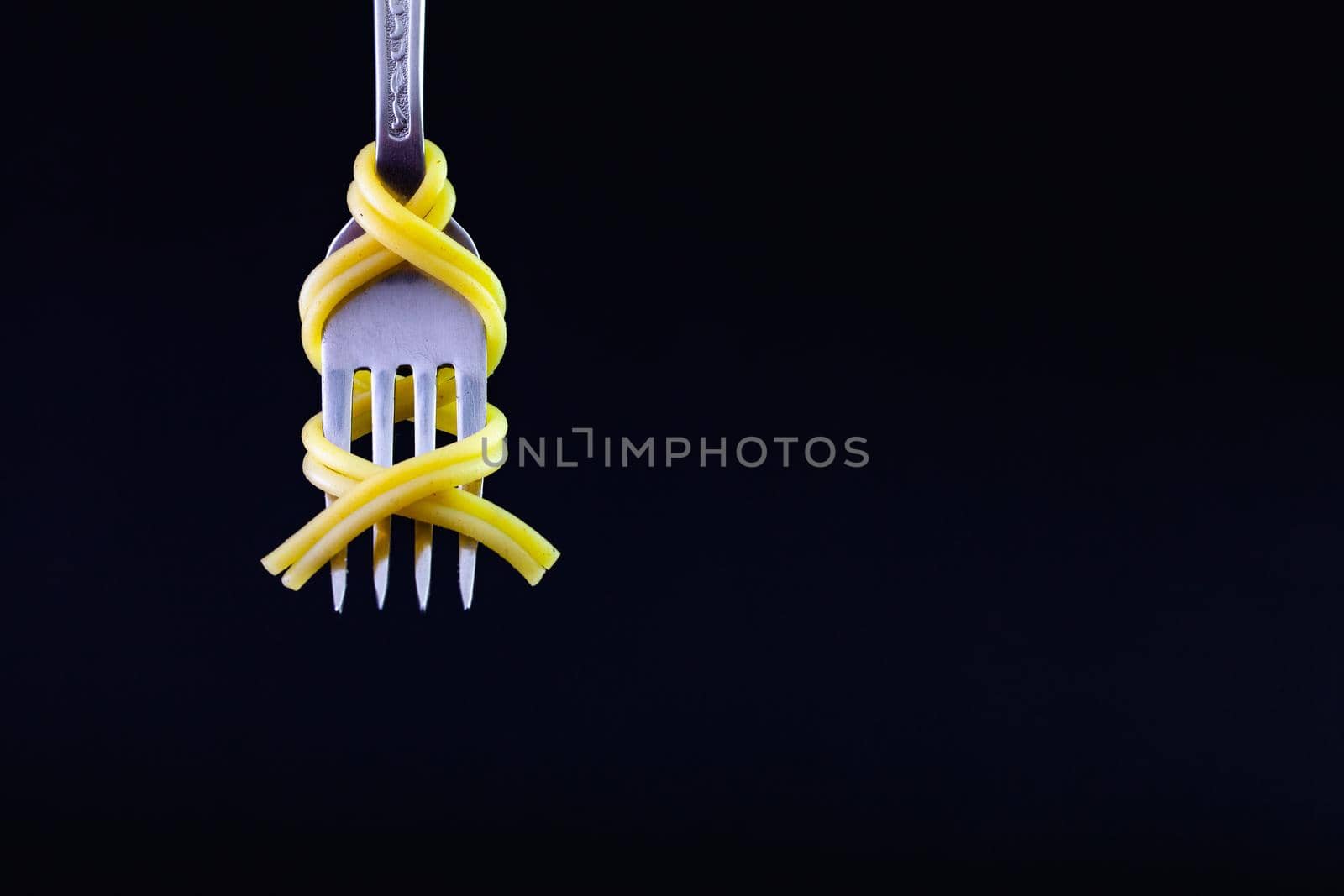 Freshly cooked pasta on a old fork on the black background. Symmetrical loop of spaghetti on an old fork.