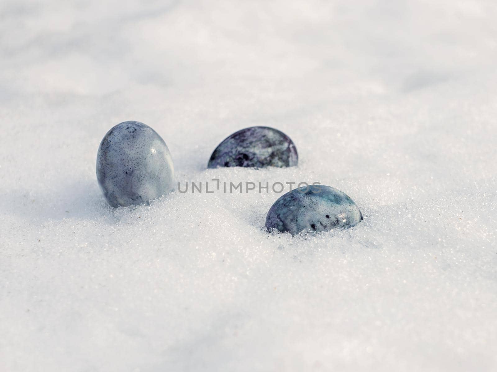 Painted chicken eggs on white snow on spring day.