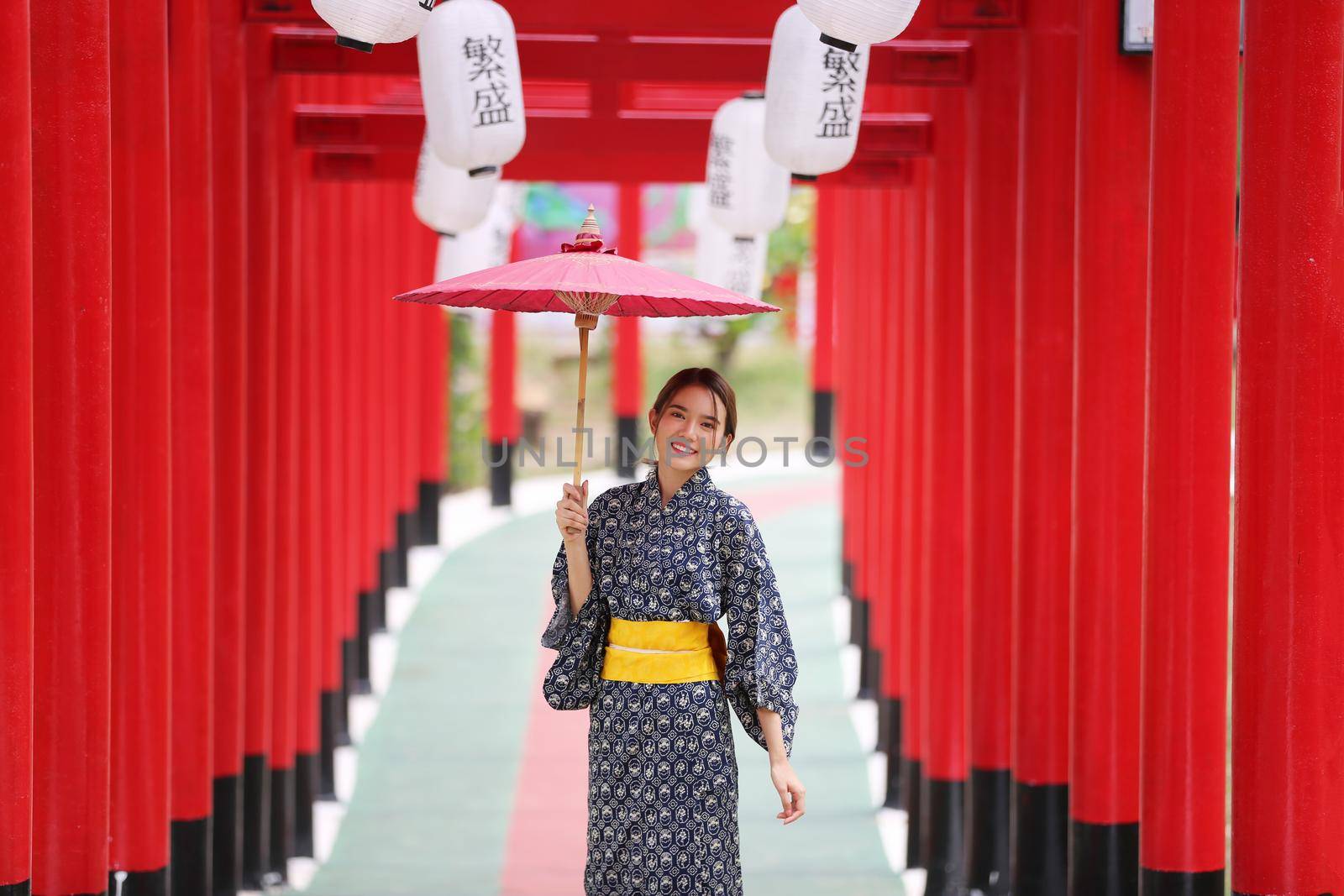 woman in kimono holding umbrella walking into at the shrine red gate, in Japanese garden.
