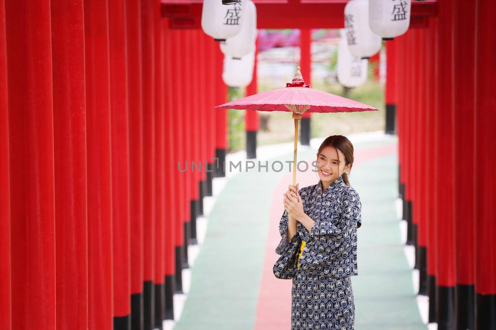 woman in kimono holding umbrella walking into at the shrine red gate, in Japanese garden.