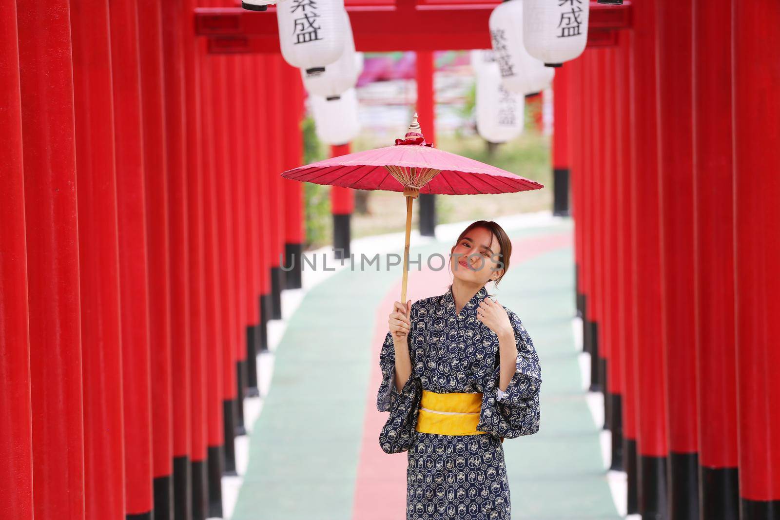 woman in kimono holding umbrella walking into at the shrine red gate, in Japanese garden.