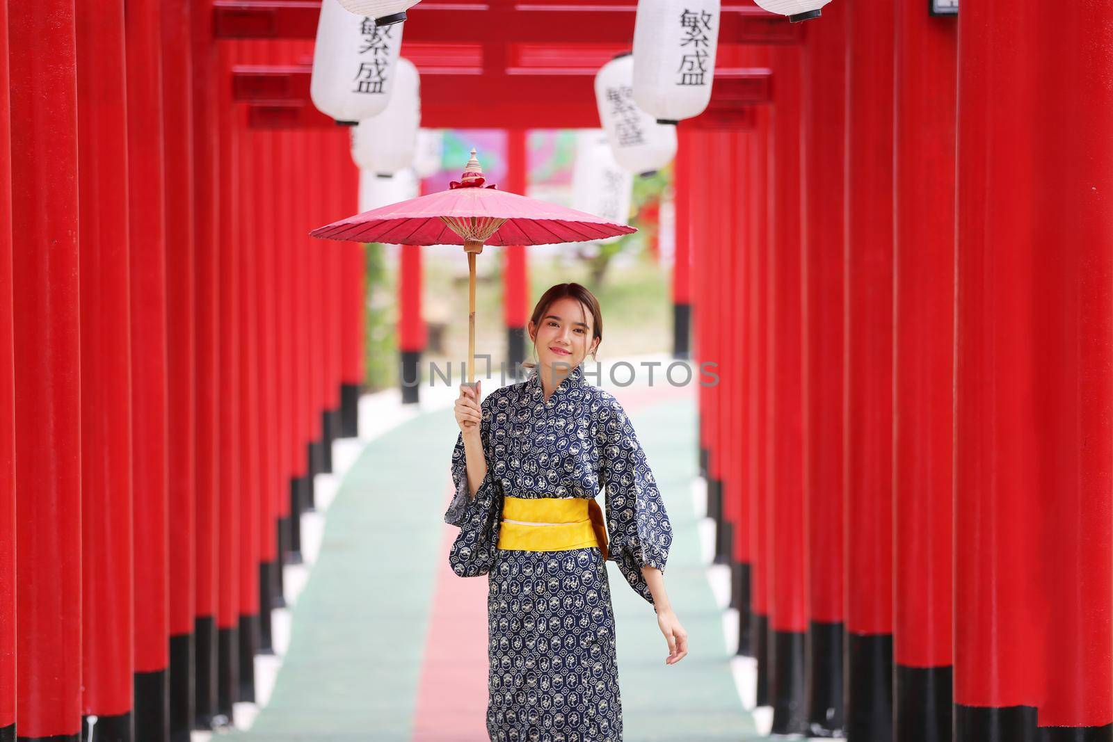 woman in kimono holding umbrella walking into at the shrine red gate, in Japanese garden.